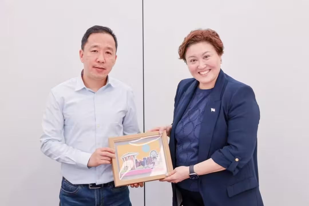 Two people stand together holding a framed illustration depicting Singapore landmarks including Marina Bay Sands and the Singapore Flyer.